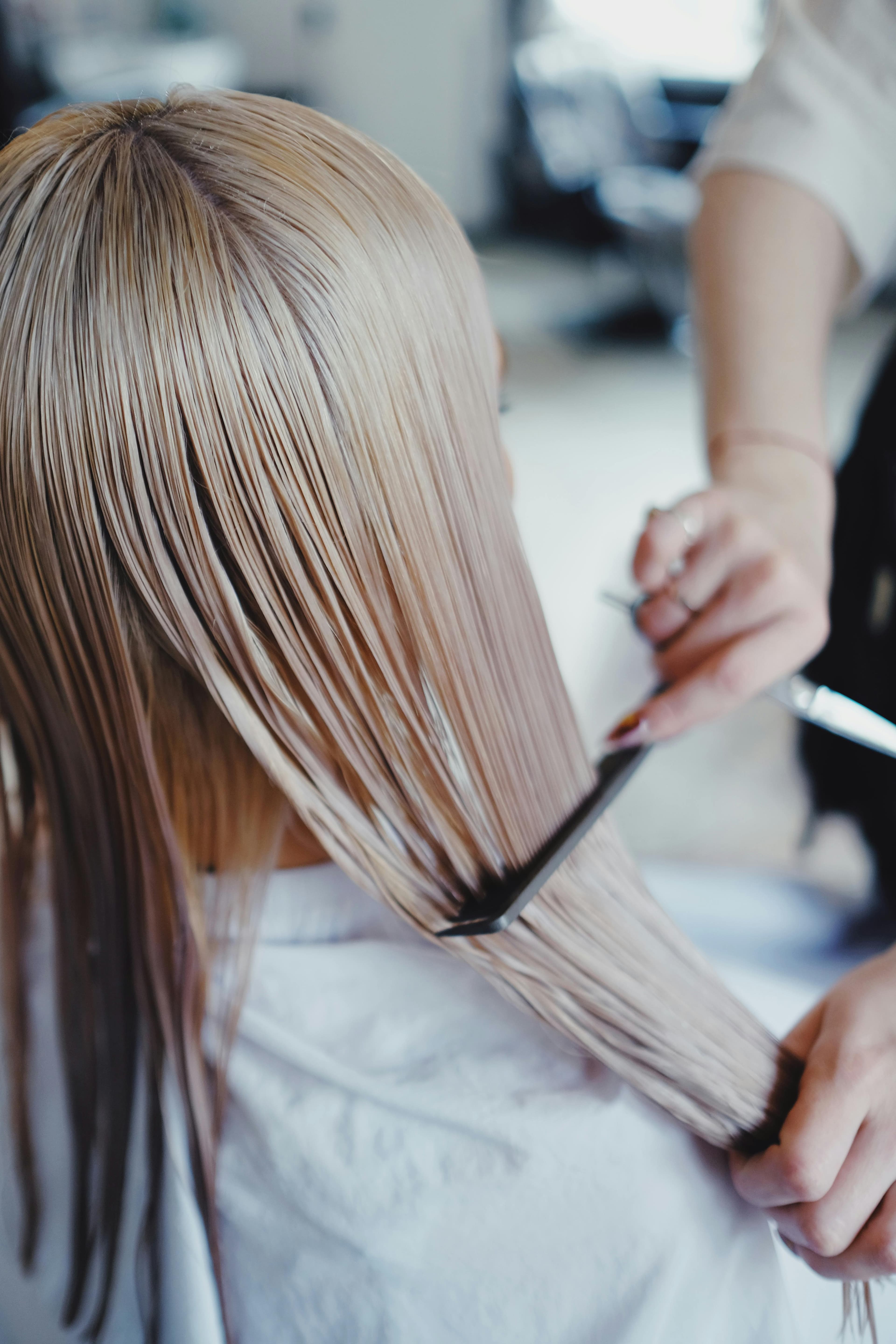 Stylist combing through sleek blonde hair after a color correction service at Hair by Beth in Brandon and Riverview FL
